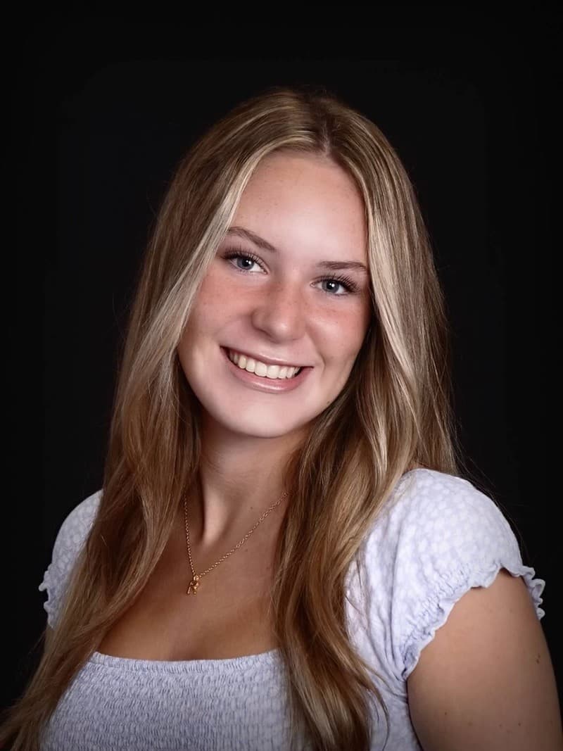 Portrait of a smiling young woman with long blonde hair against a black background.