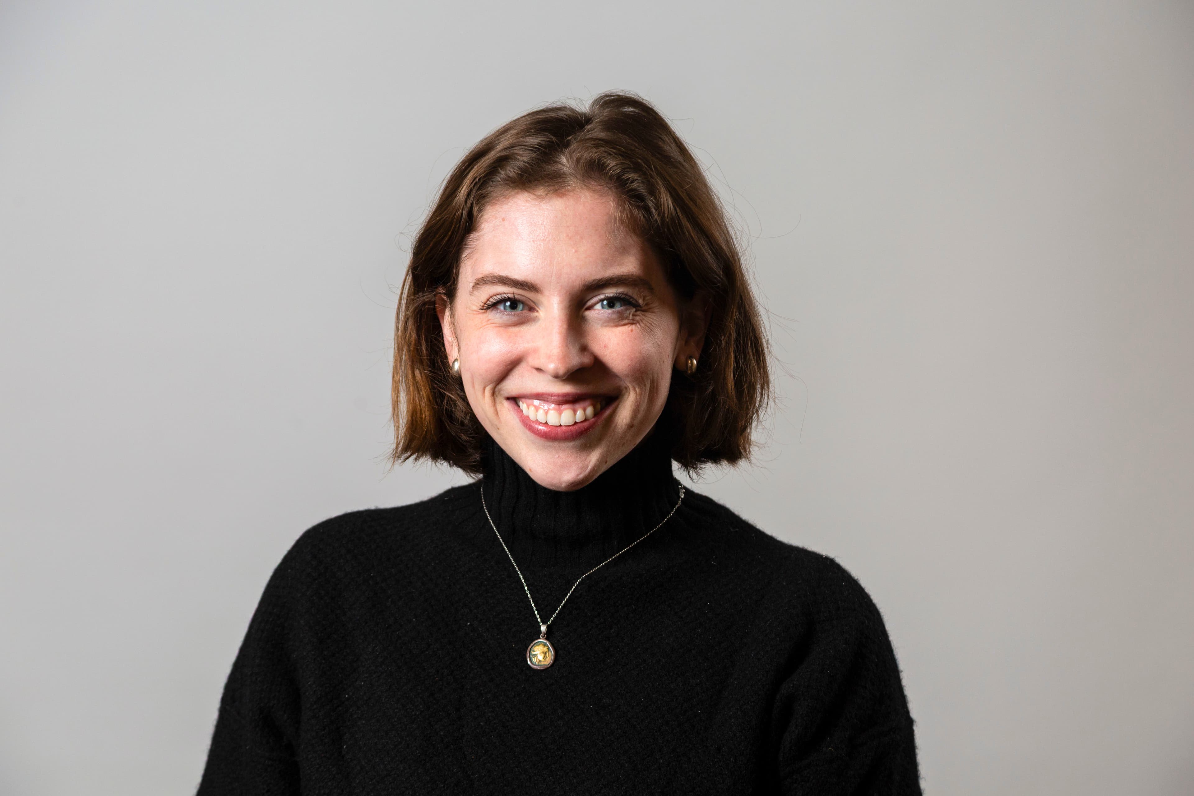 Smiling woman with short brown hair, wearing a black turtleneck and a silver necklace.