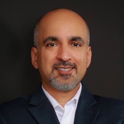 Smiling bald man with a salt-and-pepper goatee wearing a dark suit and white shirt.